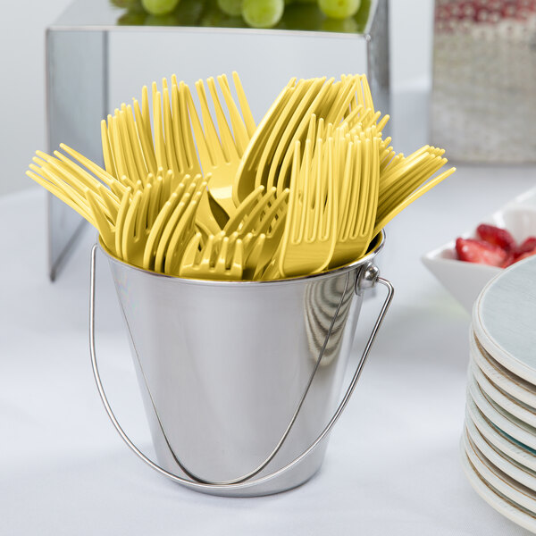 A bucket of yellow plastic forks on a table.