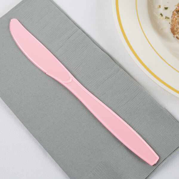 A pink knife on a napkin next to a plate of food.