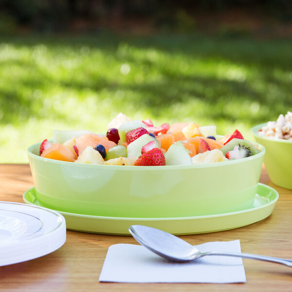 A lime melamine bowl with fruit salad on a table outdoors.