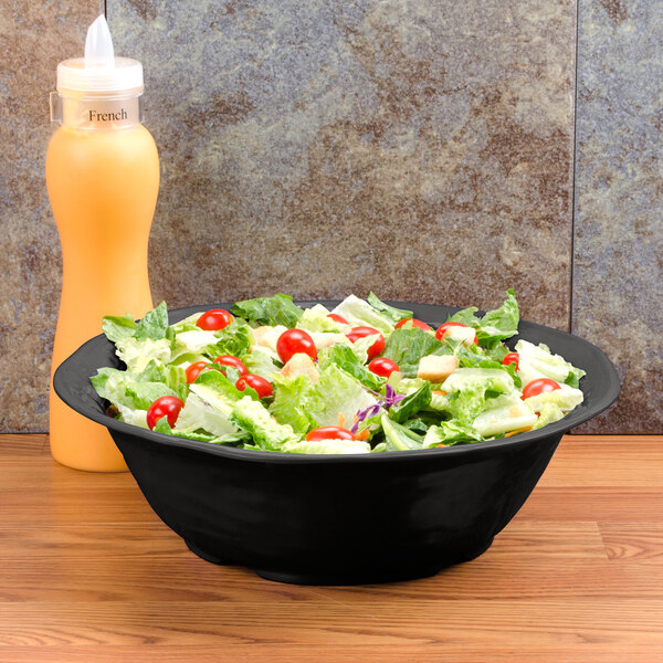 A bowl of salad in a black New Yorker serving bowl on a table.