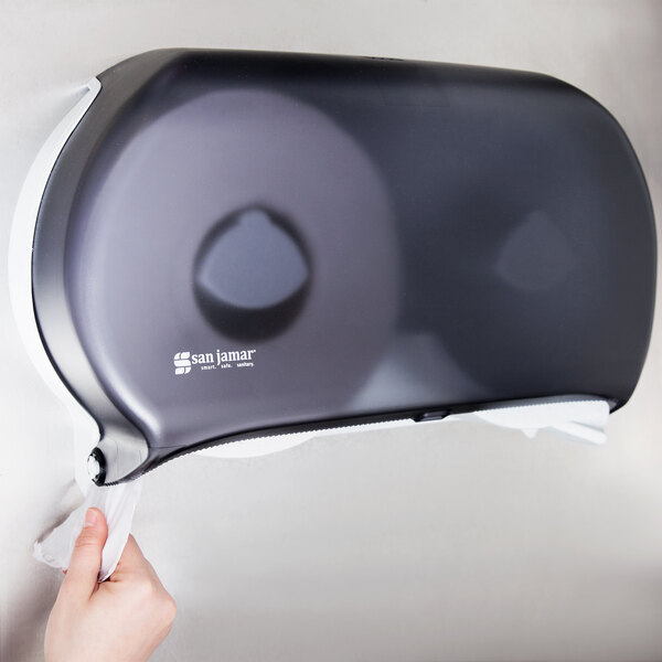A person using a San Jamar Black Pearl Twin Classic double roll toilet tissue dispenser.