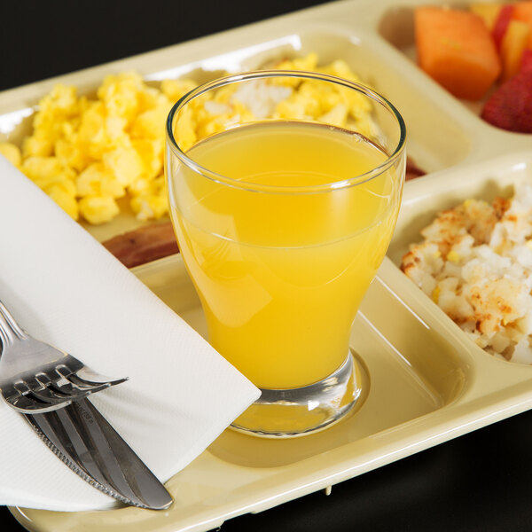 A tray with a Libbey juice glass filled with orange juice and food.