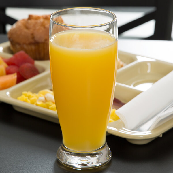 A Libbey customizable cooler glass of orange juice on a hospital tray with a muffin.