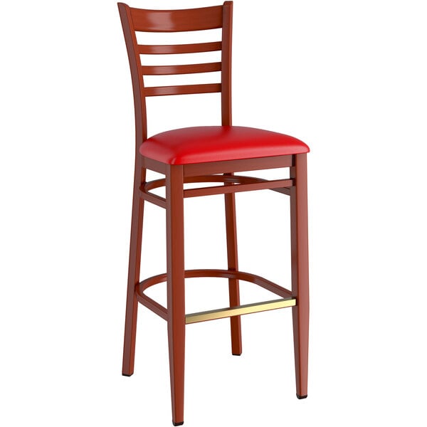 A Lancaster Table & Seating metal ladder back bar stool with a mahogany wood grain finish and red vinyl seat.