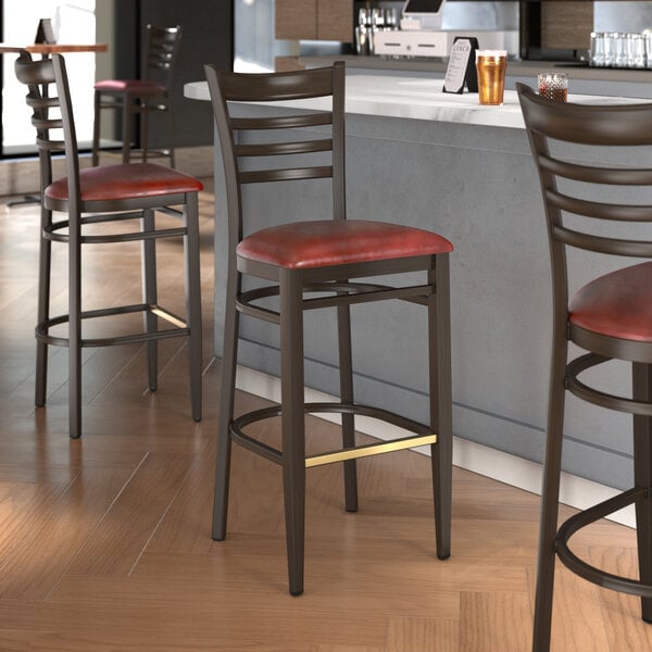 A group of Lancaster Table & Seating Spartan Series bar stools with burgundy cushioned seats at a counter.