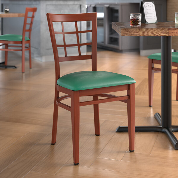 A Lancaster Table & Seating green metal chair with mahogany wood grain accents and a green vinyl cushion.