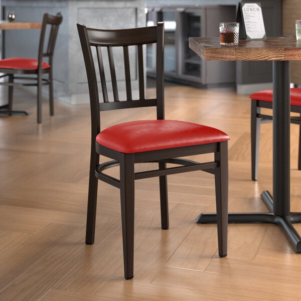 A Lancaster Table & Seating metal slat back chair with a dark walnut wood grain finish and a red vinyl seat.