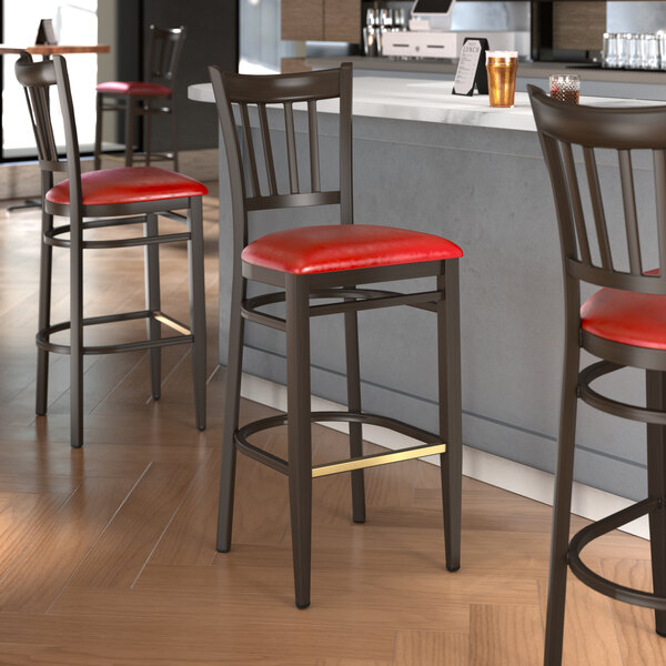 A group of Lancaster Table & Seating Spartan Series metal slat back bar stools with red vinyl seats next to a counter.