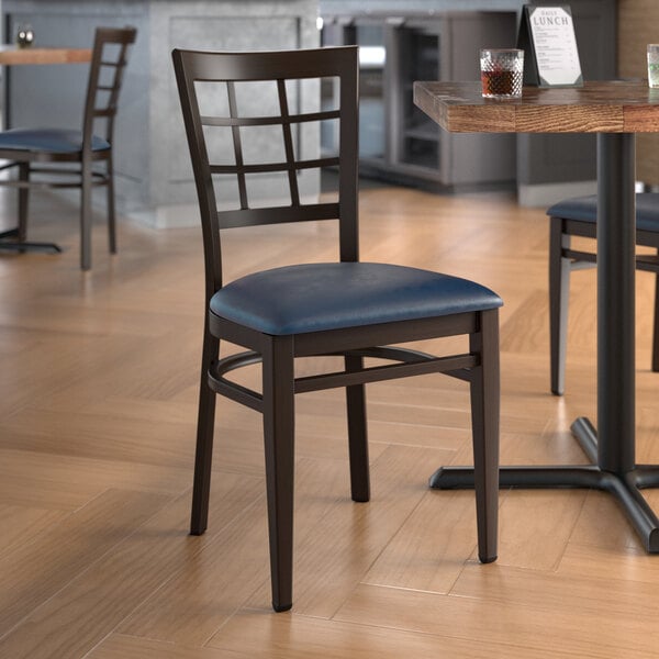 A Lancaster Table & Seating Spartan Series metal chair with dark walnut wood grain finish and navy vinyl seat on a table in a restaurant.