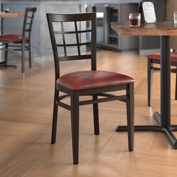 A Lancaster Table & Seating Spartan Series metal chair with dark walnut wood grain finish and burgundy vinyl seat at a restaurant table.