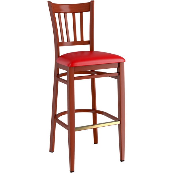 A Lancaster Table & Seating metal slat back bar stool with mahogany wood grain finish and red vinyl seat.