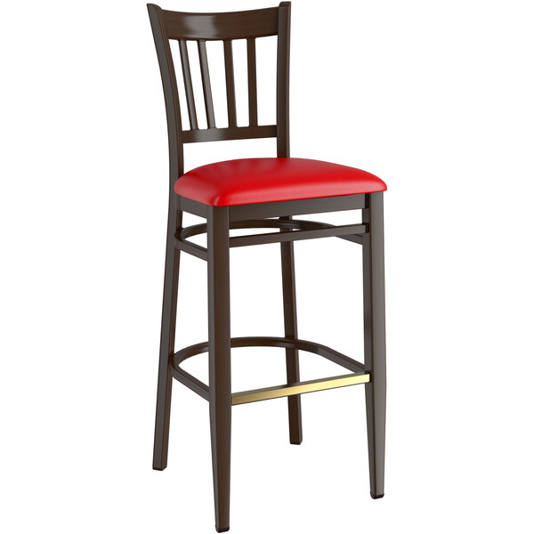 A Lancaster Table & Seating metal slat back bar stool with dark walnut wood grain finish and red vinyl seat.