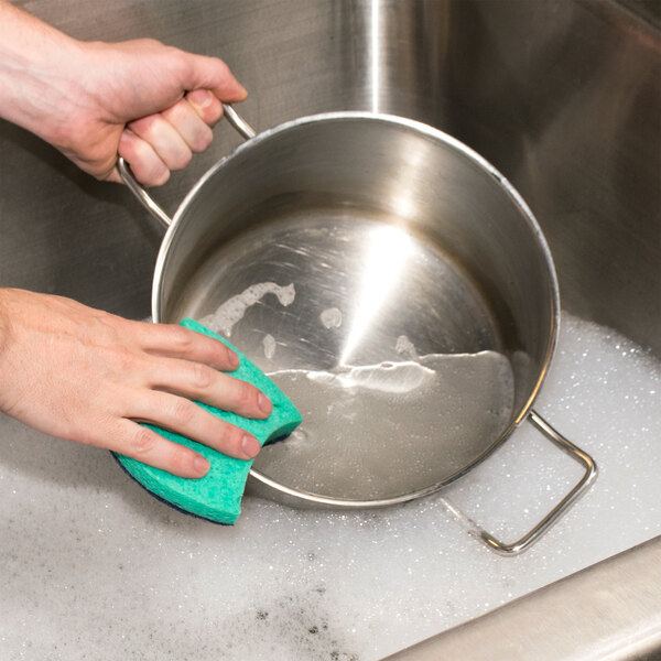 A hand holding a blue 3M Scotch-Brite Power Sponge scrubbing a pot.