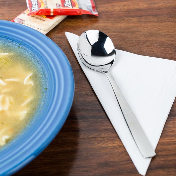 A bowl of soup and an Arcoroc stainless steel soup spoon on a napkin.