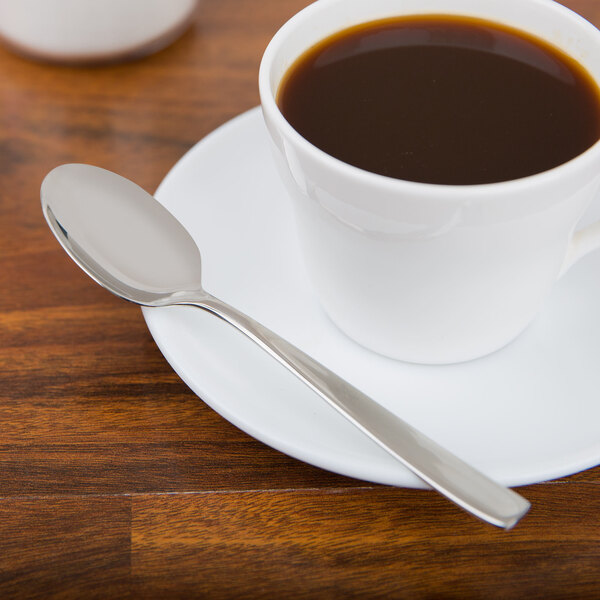 An Arcoroc stainless steel demitasse spoon on a saucer with a cup of coffee.