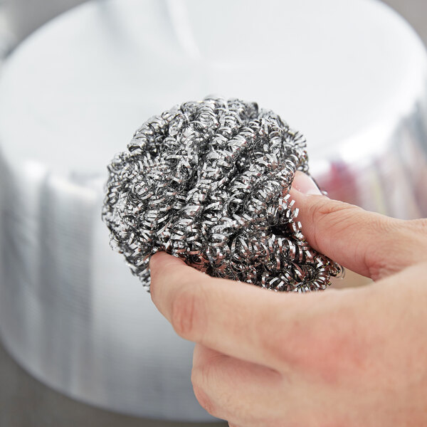 A hand holding a 3M Scotch-Brite stainless steel scrubber.