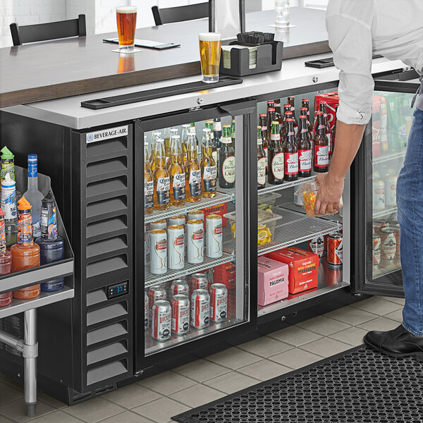 A man opening a Beverage-Air back bar refrigerator filled with drinks.
