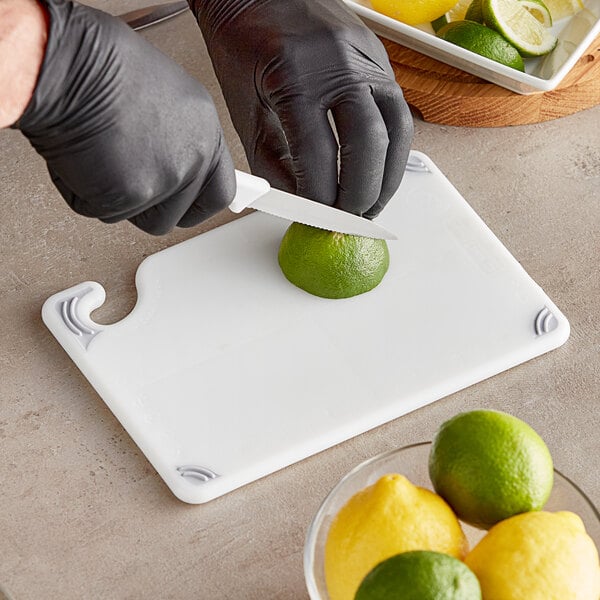 A person wearing black gloves cutting a lime on a white San Jamar bar size cutting board.