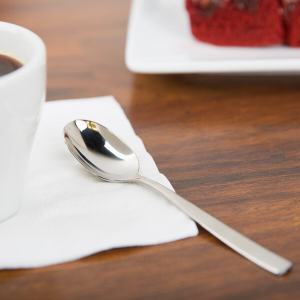An Arcoroc stainless steel teaspoon on a napkin next to a cup of coffee.