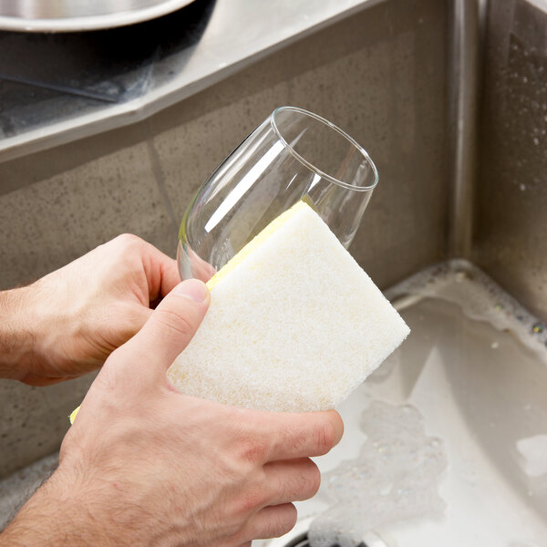 A person holding a 3M Scotch-Brite light-duty scrub sponge over a sink.