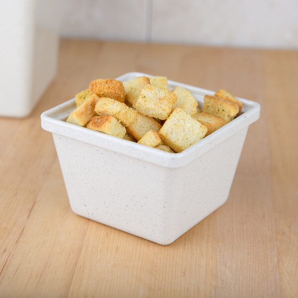 A GET white melamine square crock filled with croutons on a wood surface.