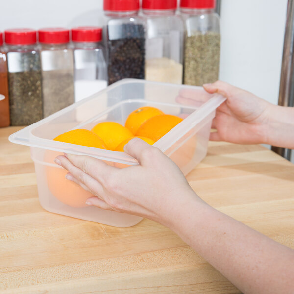A person holding a Cambro translucent polypropylene food pan full of oranges.