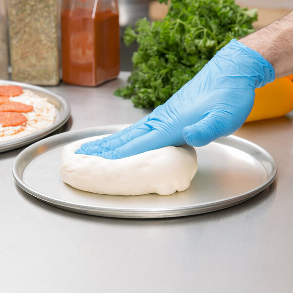 A person wearing blue gloves holding dough on an American Metalcraft deep dish pizza pan.
