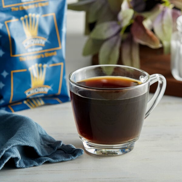 A glass of Emperor's Blend coffee next to a Crown Beverages coffee packet.