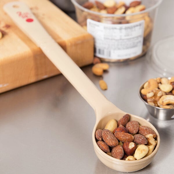 A Carlisle long handle solid portion spoon with nuts on a counter.