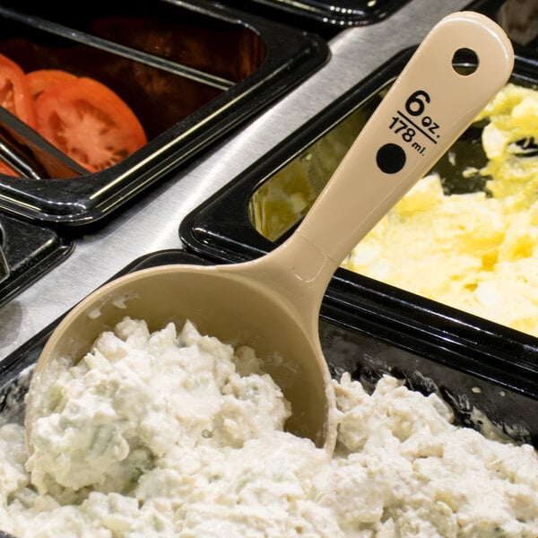 A Carlisle beige and black color-coded portion spoon with a scoop of food in a container.