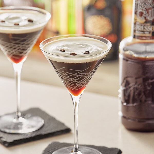 A close-up of two martini glasses filled with brown liquid with brown liquid drizzled in one.