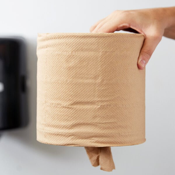 A person holding a brown natural kraft coreless center pull paper towel roll.