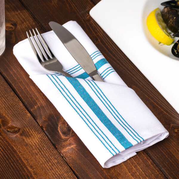 A plate with a Snap Drape Belize Blue Bistro striped cloth napkin, with a knife and fork.