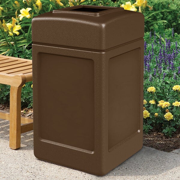 A brown Commercial Zone PolyTec waste container next to a bench.