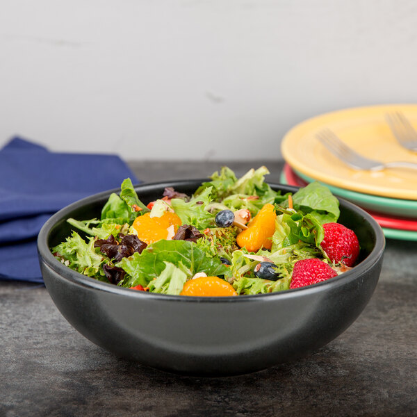 A black Hall China large bistro bowl filled with salad, oranges, and berries.
