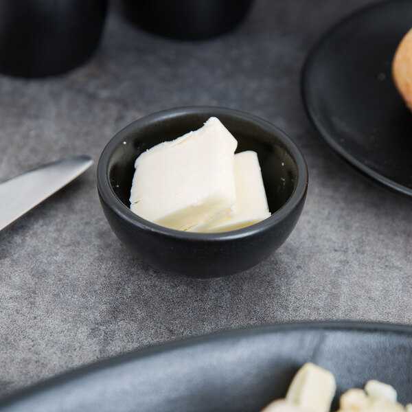 A black Hall China ramekin filled with butter on a table with a knife.