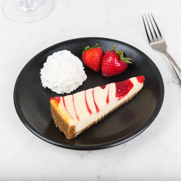 A slice of cheesecake with strawberries on a Hall China Foundry black coupe plate.
