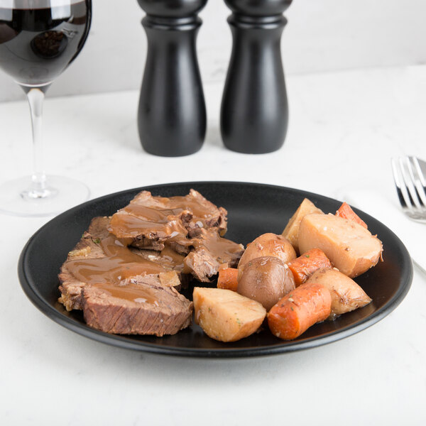 A Hall China black round coupe plate with meat and vegetables.
