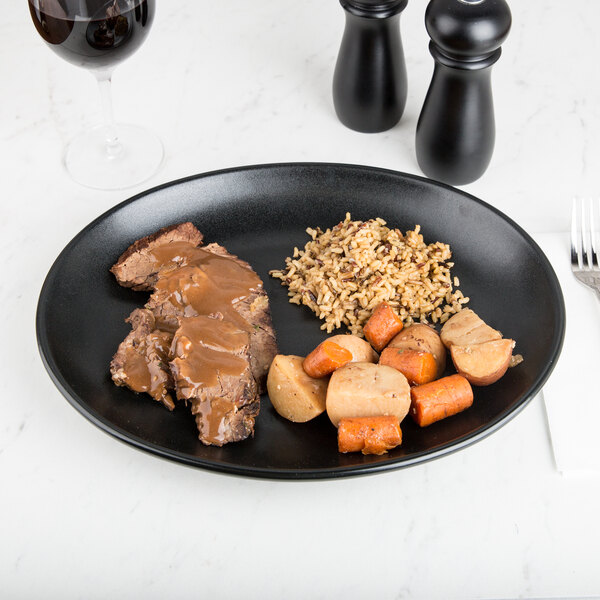 A black Hall China oval platter with meat and rice and vegetables on it.
