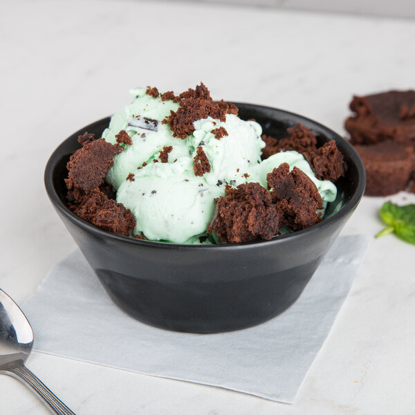 A Hall China black bowl filled with mint chocolate chip ice cream and brownies with a spoon.