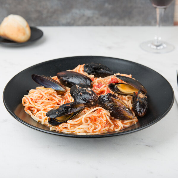 A Hall China black bowl filled with spaghetti and mussels in sauce.