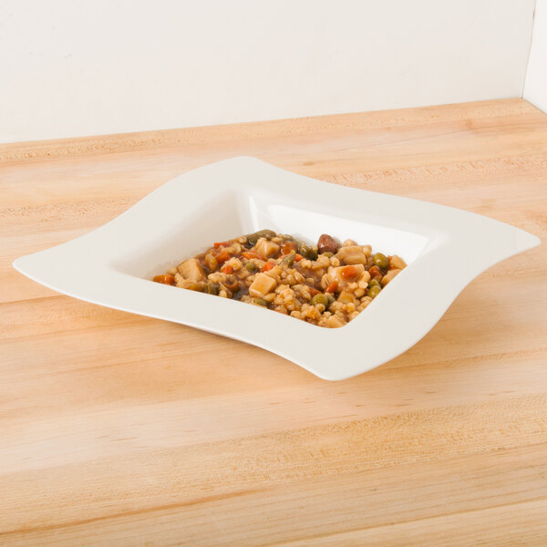 A Fineline Wavetrends ivory plastic bowl filled with food on a table.