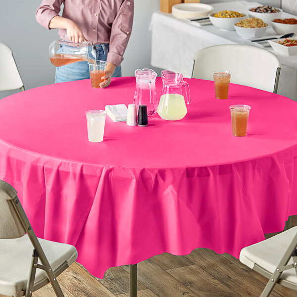 A woman pouring yellow liquid into a glass on a table with a hot magenta pink tablecloth.