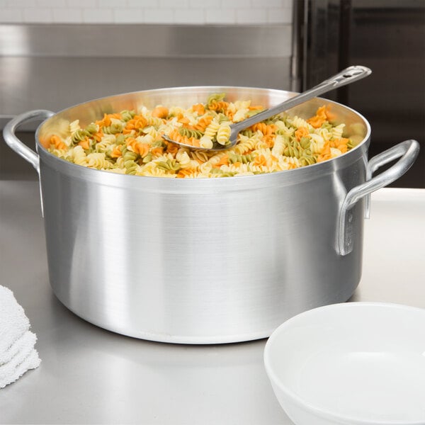 A Vollrath aluminum pot filled with pasta and vegetables on a table.