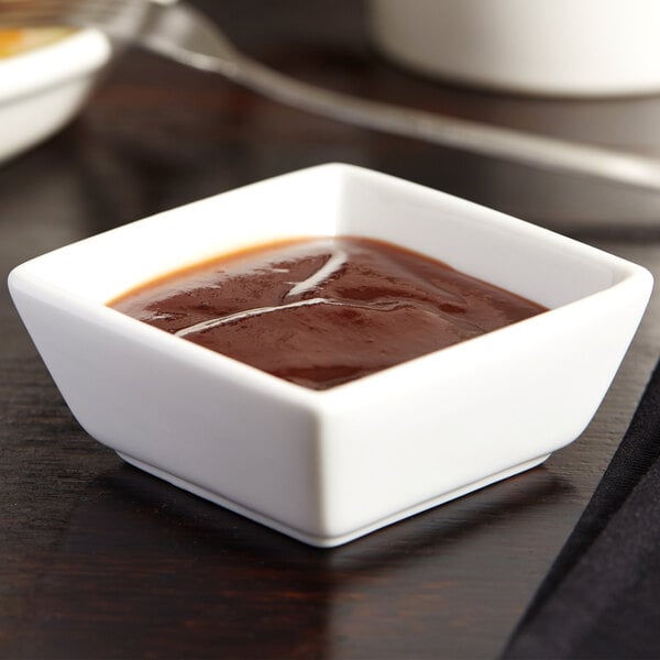 A Libbey square porcelain dipping bowl filled with chocolate sauce on a table.