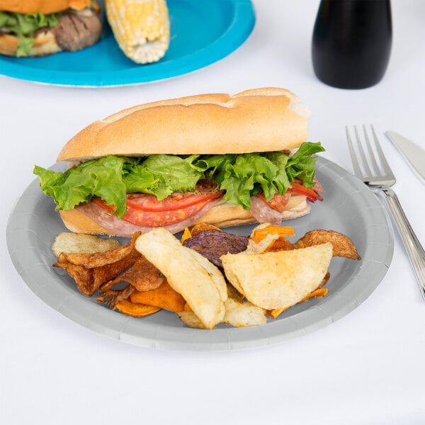 A sandwich with lettuce and tomato on a Creative Converting shimmering silver paper plate with potato chips.