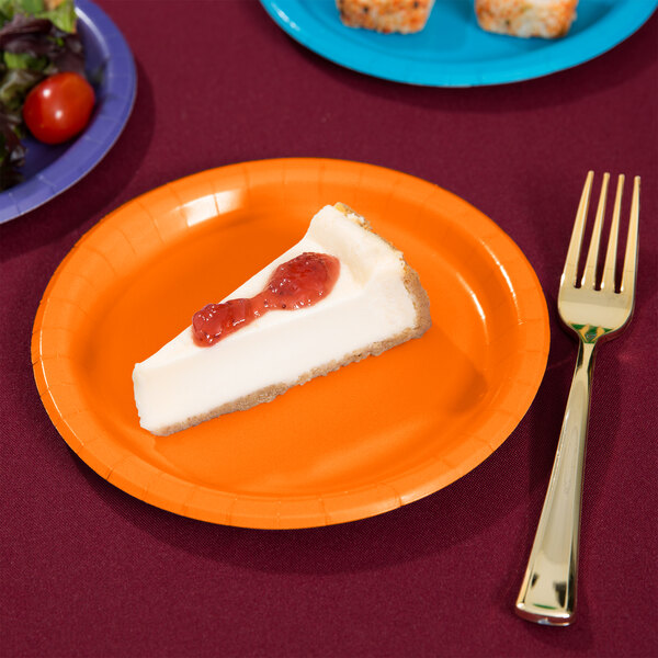 A piece of cheesecake with strawberry jam on an orange paper plate with a fork.