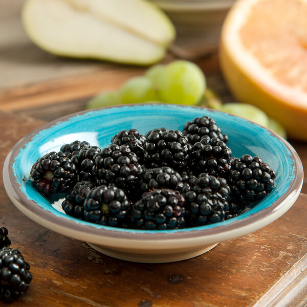 A bowl of blackberries in a Carlisle aqua melamine bowl on a table.