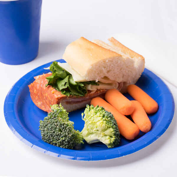 A Creative Converting cobalt blue paper plate with a sandwich, carrots, and broccoli on it.