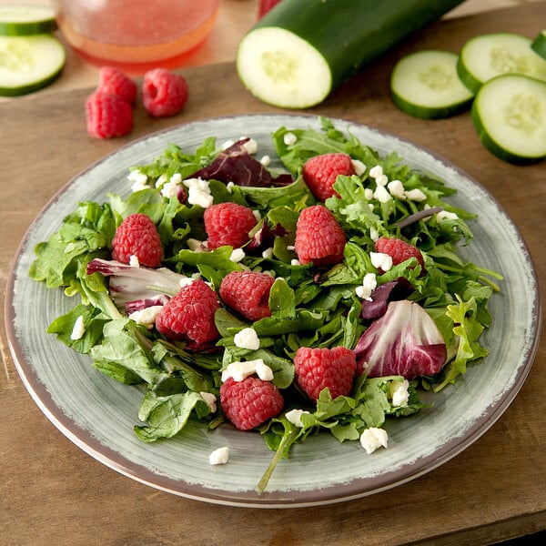 A Carlisle round smoke melamine salad plate with salad, raspberries, and cucumbers.